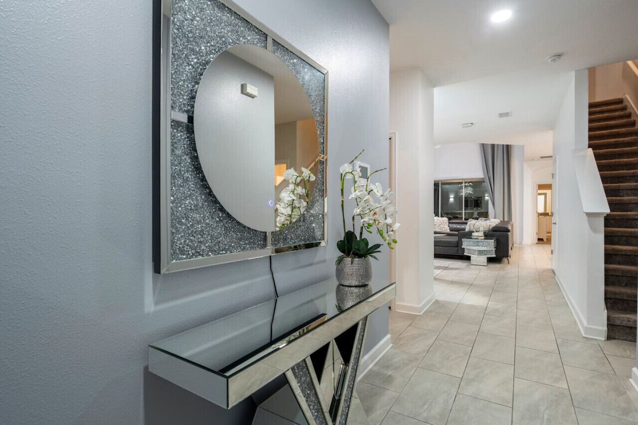 A modern interior with a large mirror, a console table, and a staircase leading to a living area.