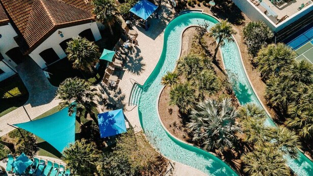 An aerial view of a resort with multiple swimming pools, palm trees, and lounge areas.