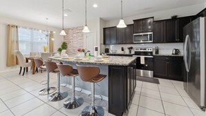 A modern kitchen with dark cabinets, stainless steel appliances, and a central island with bar stools.