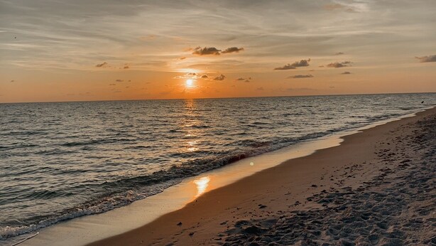 Een strand met golven, een zonsondergang en een heldere lucht.