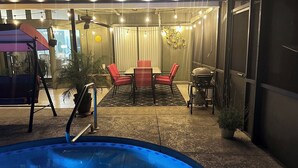Een terras buiten met een zwembad, zitplaatsen en een barbecue.