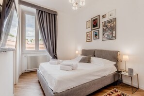A bedroom with a bed, bedside lamps, a radiator, and a window with curtains.