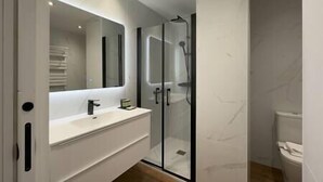 Une salle de bain moderne avec une douche à parois de verre, un grand miroir et un meuble-lavabo blanc.