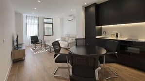 Un salon moderne avec une table ronde, des chaises noires, un canapé et un téléviseur.