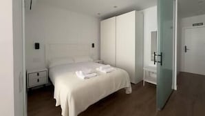 A modern bedroom with a bed, bedside tables, a wardrobe, and a glass door leading to another room.