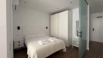 A modern bedroom with a bed, bedside tables, a wardrobe, and a glass door leading to another room.