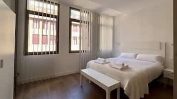 A bedroom with a bed, a bench, and two windows with blinds.