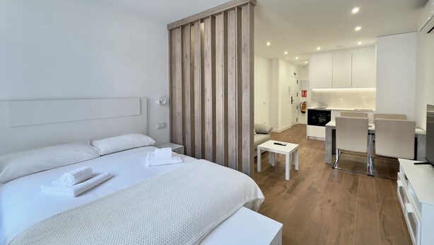 A modern hotel room with a large bed, a small bedside table, a wooden partition, a kitchenette, and a dining area. - Apartment in Madrid Centro (Madrid)