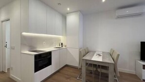 A modern kitchen with white cabinetry, a built-in oven, and a dining area with a table and chairs. - Apartment in Madrid Centro (Madrid)