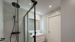 A modern bathroom with a glass-enclosed shower, a white sink, and a large mirror. - Apartment in Madrid Centro (Madrid)
