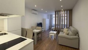 A modern living room with a sofa, a dining table, and a kitchen area with a refrigerator and a sink. - Apartment in Madrid Centro (Madrid)