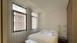 A hotel room with a large bed, a bedside table, and a window with blinds. - Apartment in Madrid Centro (Madrid)