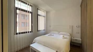 A hotel room with a large bed, a bedside table, and a window with blinds.