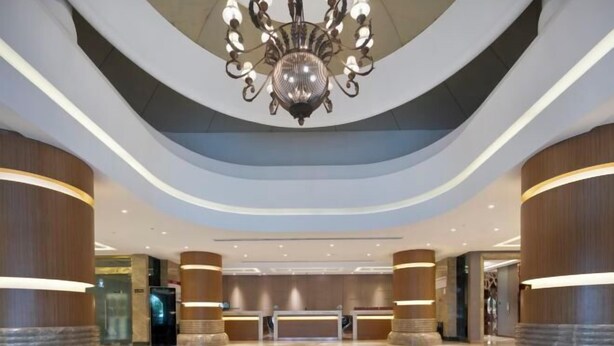 A modern lobby with a central reception desk, a large chandelier, and curved ceiling design. - Pudong Fute Hotel (Xiepu Road Subway Station) (Shanghai)