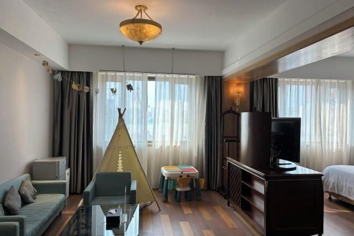 A hotel room with a sofa, a glass coffee table, a television, a bed, a small table with chairs, and a tent-like structure.