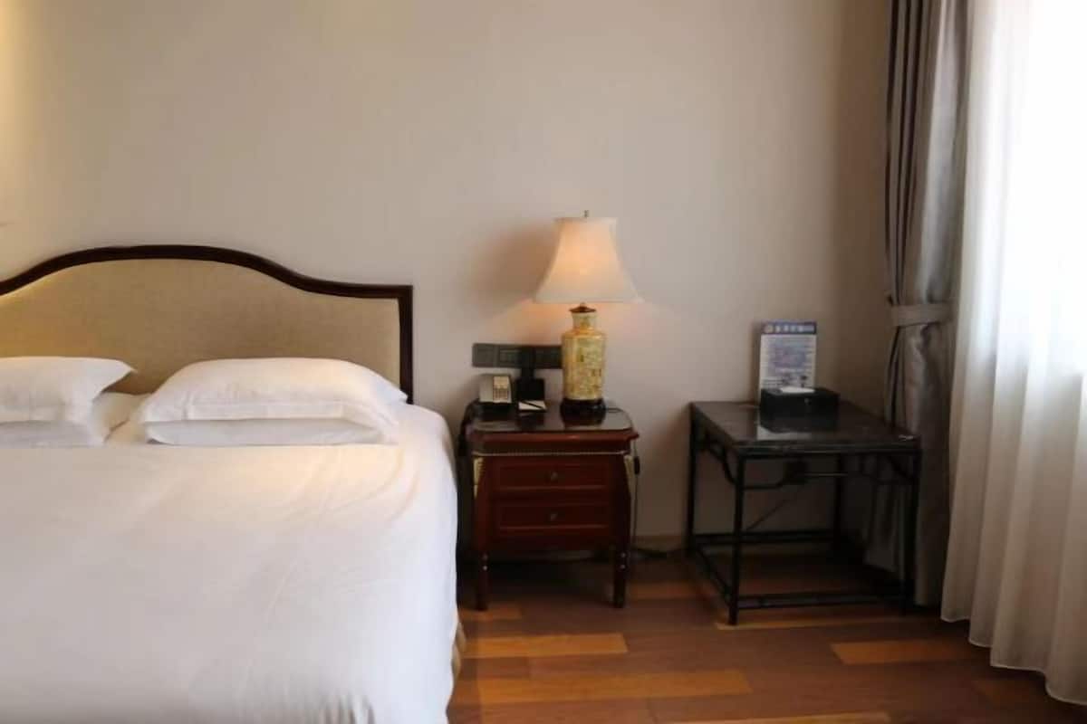 A hotel room with a bed, a nightstand with a lamp, a small table, and a sign on the wall.