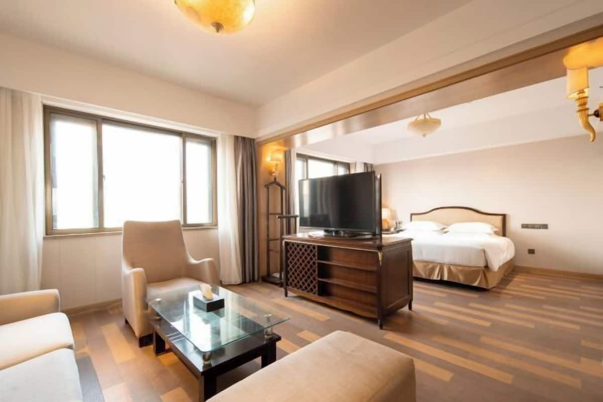 A hotel room with a bed, a TV, a sofa, a coffee table, and a large window.