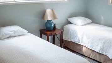 A hotel room with two beds, a nightstand with a lamp, and a window providing natural light.