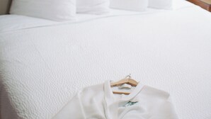Ein ordentlich bezogenes Bett mit weißer Bettwäsche und Kissen, ein gerahmtes Kunstwerk an der Wand und ein Nachttisch mit Lampe.