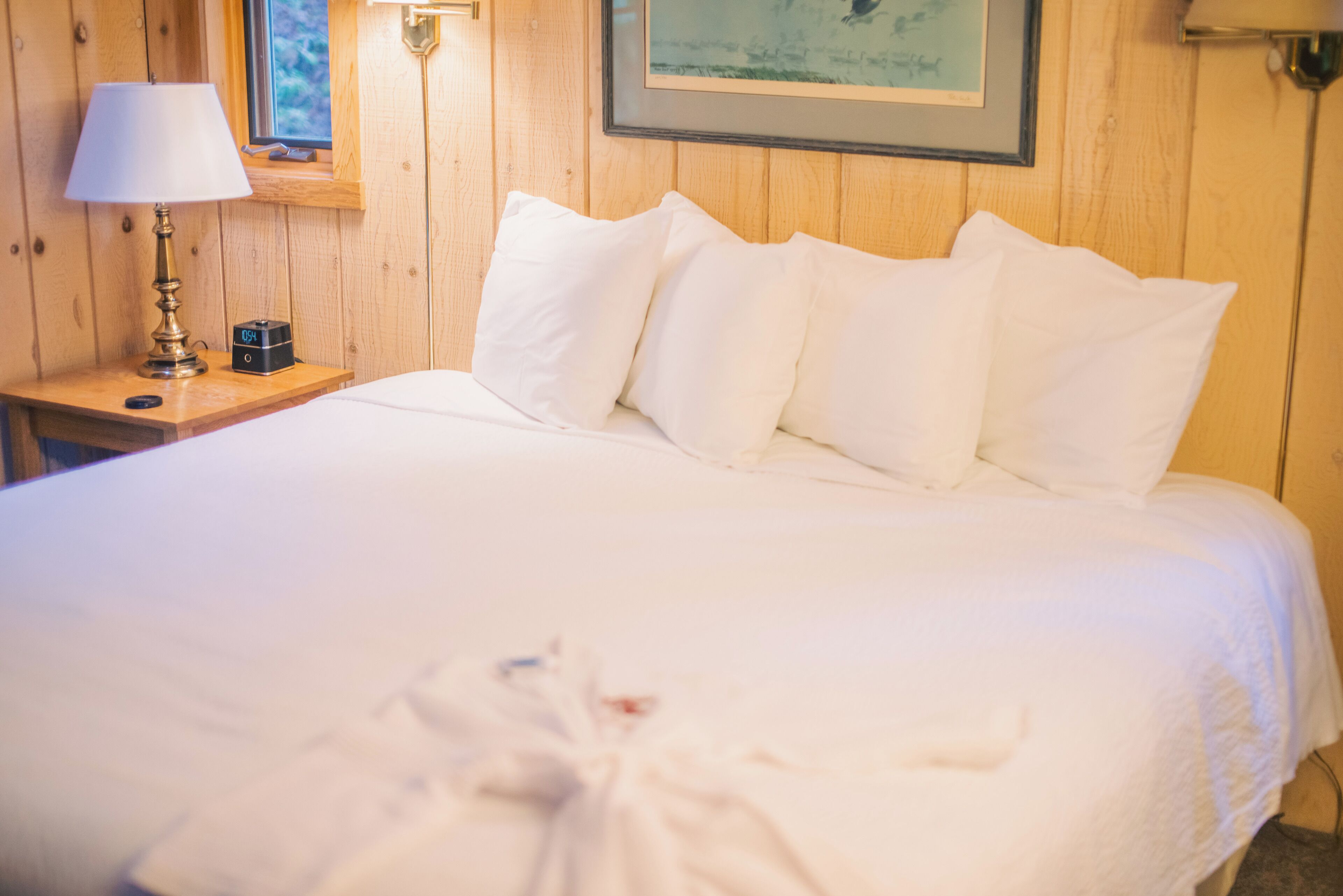 A neatly made bed with white linens in a wooden room.