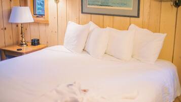 A neatly made bed with white linens in a wooden room.