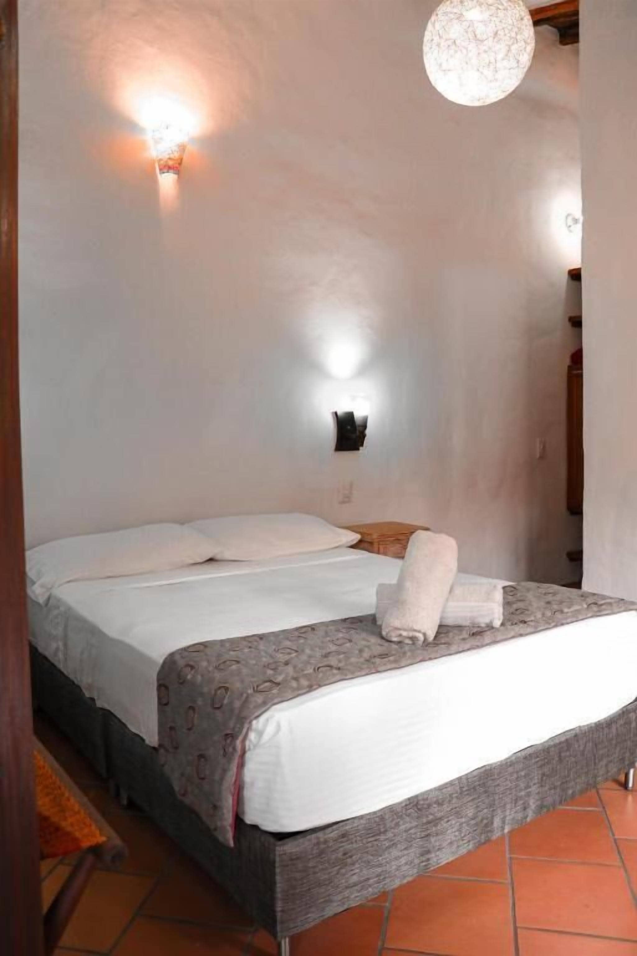 A bedroom with a bed, a wall-mounted light, and a hanging light fixture.