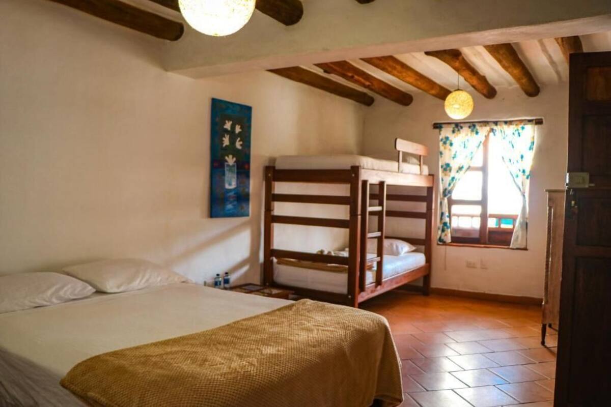 Een kamer met een enkel bed, een stapelbed, een houten plafond en een raam met gordijnen.