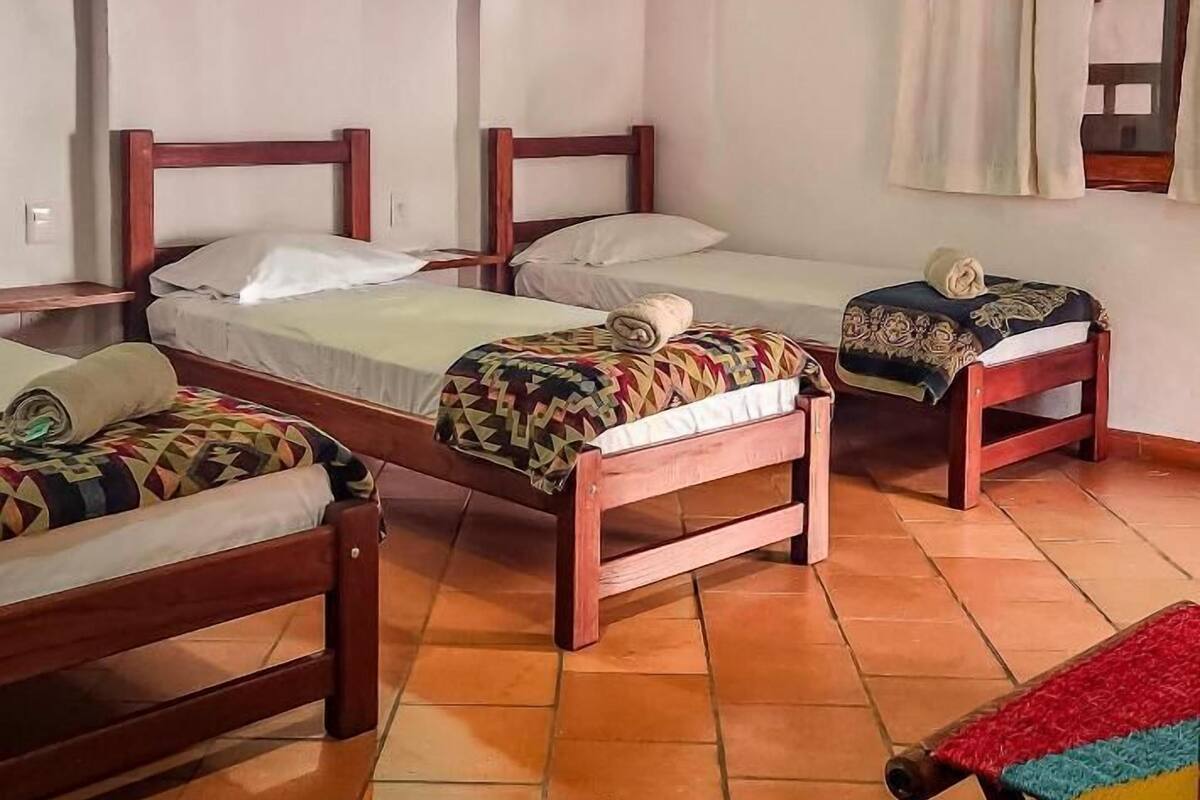 Een kamer met drie houten bedden, een betegelde vloer en een raam met gordijnen.