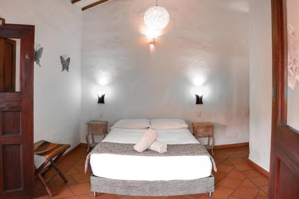Een slaapkamer met een bed, twee nachtkastjes, een hanglamp en een houten deur.
