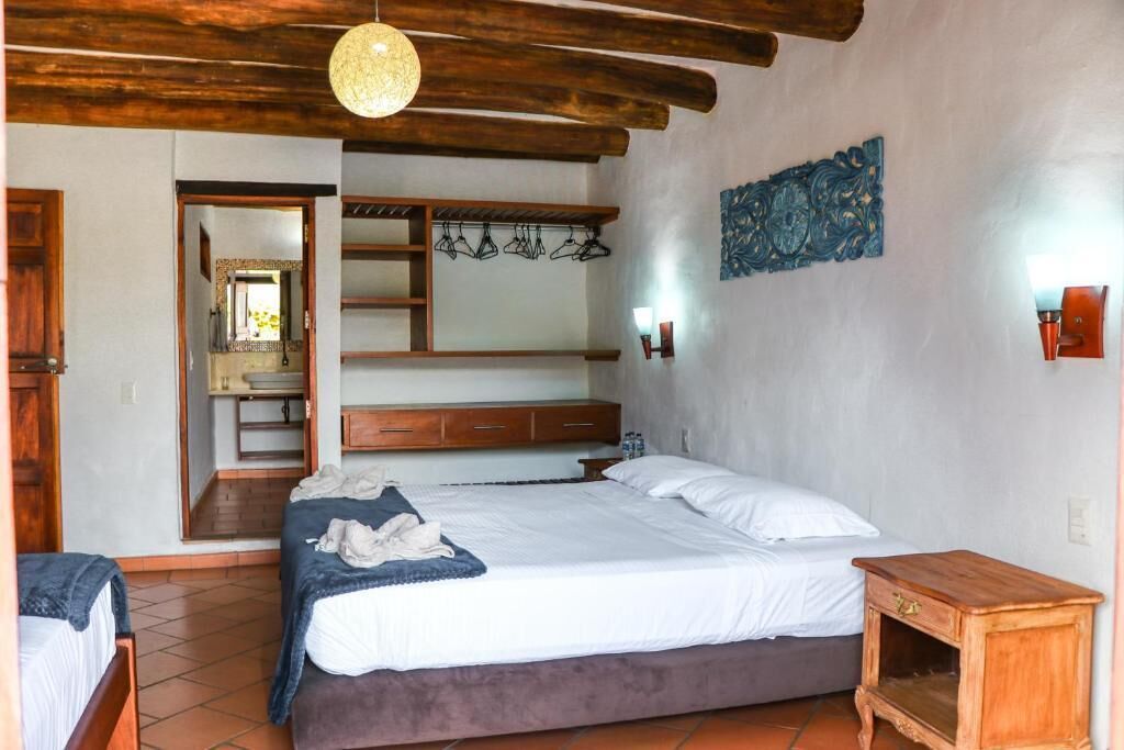 A bedroom with a bed, wooden headboard, a hanging light fixture, a wall-mounted shelf, and a small wooden nightstand.