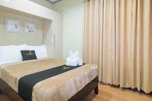 Een hotelkamer met een bed, hoofdeinde, raam met gordijnen en een muur met ingekaderde kunstwerken.