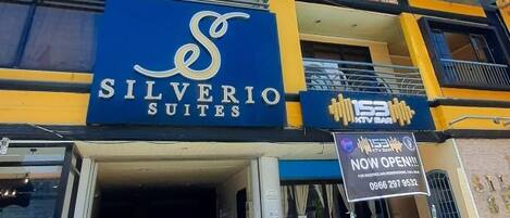 A hotel entrance with a sign for 'Silverio Suites' and a 'NOW OPEN' sign.