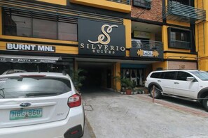 Een hotelentree met een bordje voor 'Silverio Suites' en een parkeerplaats met auto's.