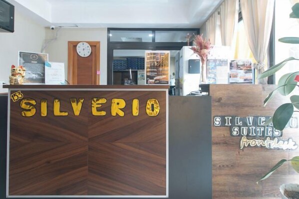 Een receptiebalie met de naam 'SILVERIO SUITES' en een klok erboven.