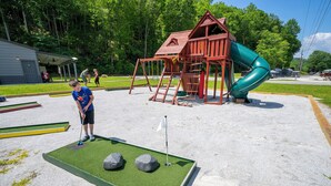 Un campo de minigolf con una casa club roja y un tobogán verde al fondo.
