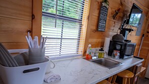 Cocina con encimera de mármol, pileta, tetera y tostadora. Hay taburetes de madera y una ventana con persianas.
