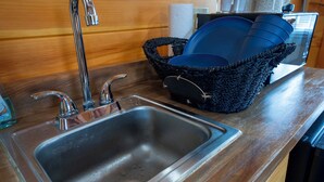 Een keuken met een roestvrijstalen spoelbak, twee kraanwerk, een zwart geweven mand met blauw servies, en een houten aanrecht.