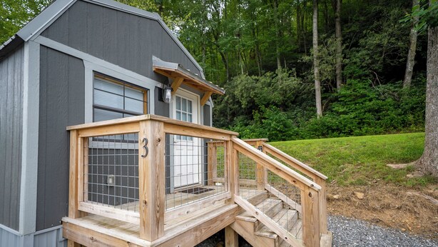A wooden deck with a metal gate leading to a house with a grey exterior and a window with blinds. - 1 Room Cabin- " The Garage" (Robbinsville)