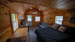 A cozy cabin interior with a wooden ceiling, a bed with patterned pillows, a small table, and a kitchenette. - 1 Room Cabin- " The Garage" (Robbinsville)