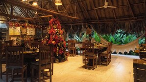 Ein Restaurant mit einem Strohdach, Holzmöbeln und hängenden Korbtischen.