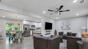 A modern living room with a sectional sofa, a dining area with a table and chairs, a kitchen with white cabinets, a flat-screen TV mounted on the wall, and a ceiling fan. - Rare Find Atlanta Retreat, this weekend just opened, Near Airpott+EV Charger (Atlanta)