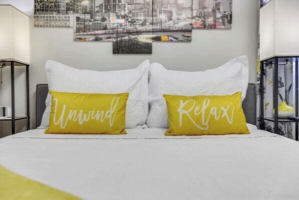 Un lit avec une literie blanche et deux oreillers jaunes sur lesquels sont brodés les mots « Détendez-vous » et « Relaxez-vous ».