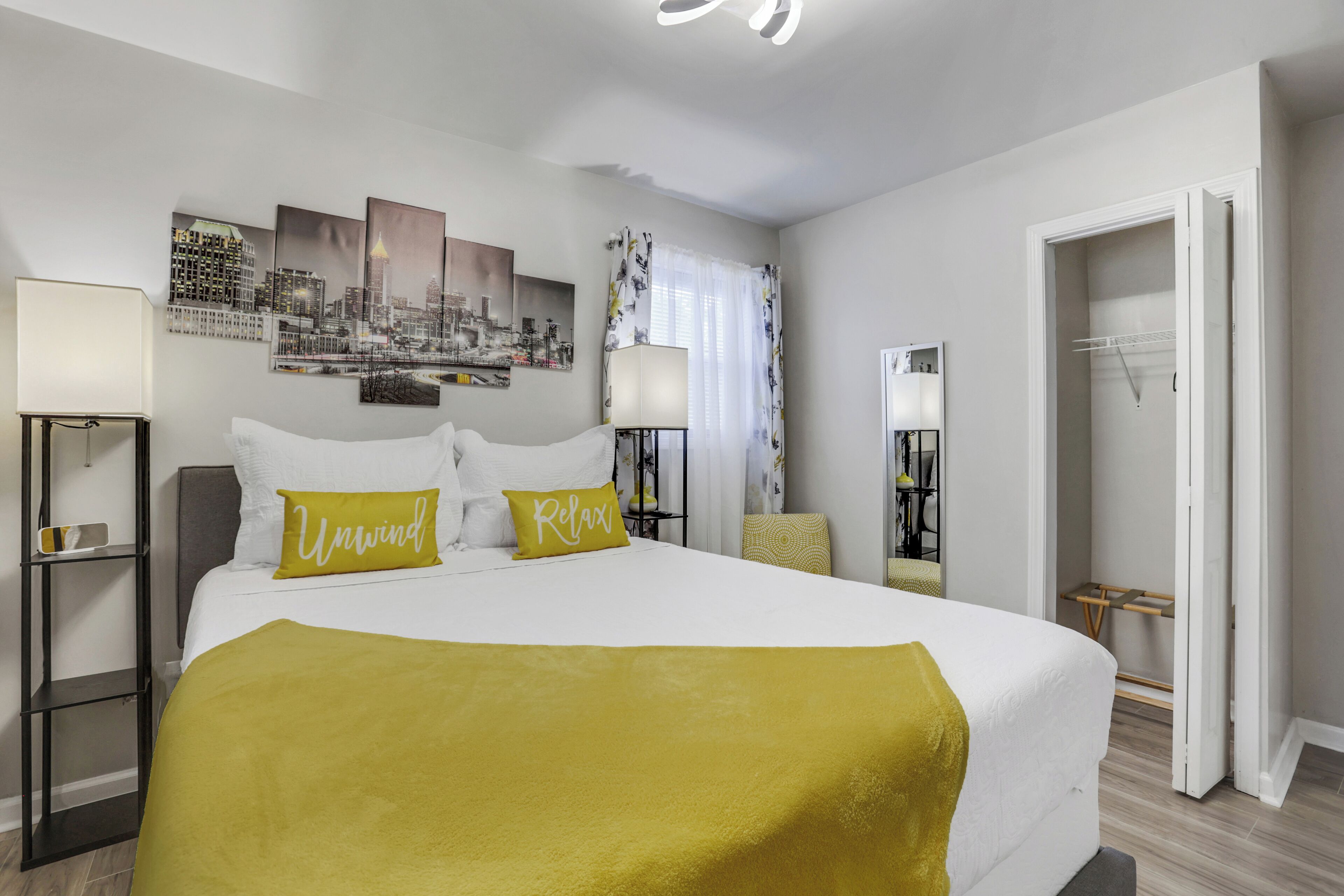 Ein Hotelzimmer mit einem großen Bett, zwei Nachttischen, einem Stadtbild an der Wand, einer Tür zum Badezimmer und einem Spiegel.
