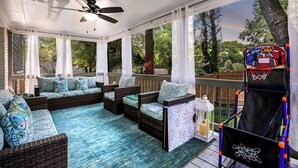 A covered outdoor area with wicker furniture, a basketball hoop, and a view of the surrounding trees. - Rare Find Atlanta Retreat, this weekend just opened, Near Airpott+EV Charger (Atlanta)