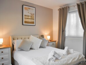 A neatly made bed with white linens, a headboard, and a bedside table with a lamp. - 3 bedroom accommodation in Filey (Filey)