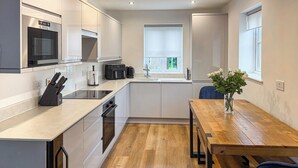 A modern kitchen with a built-in oven, a coffee maker, and a dining area with a wooden table and chairs. - 3 bedroom accommodation in Filey (Filey)
