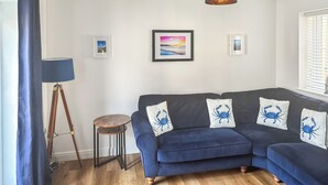 A living room with a dark blue sofa, a standing lamp, and framed pictures on the wall. - 3 bedroom accommodation in Filey (Filey)