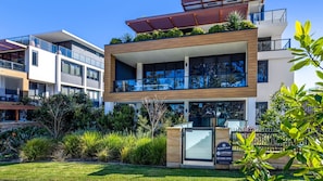 A modern multi-story residential building with balconies, large windows, and a well-maintained garden.