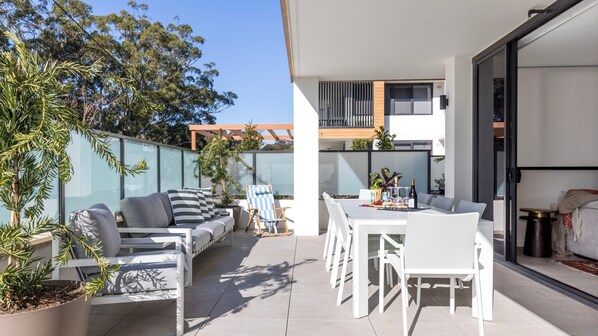 A modern outdoor patio with a dining area, seating, and potted plants. - Iggy's Retreat Huskisson by Latitude South Coast (Huskisson)