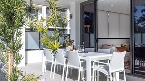 A modern outdoor dining area with white chairs and a table set for two, featuring a bottle of champagne and glasses. - Iggy's Retreat Huskisson by Latitude South Coast (Huskisson)